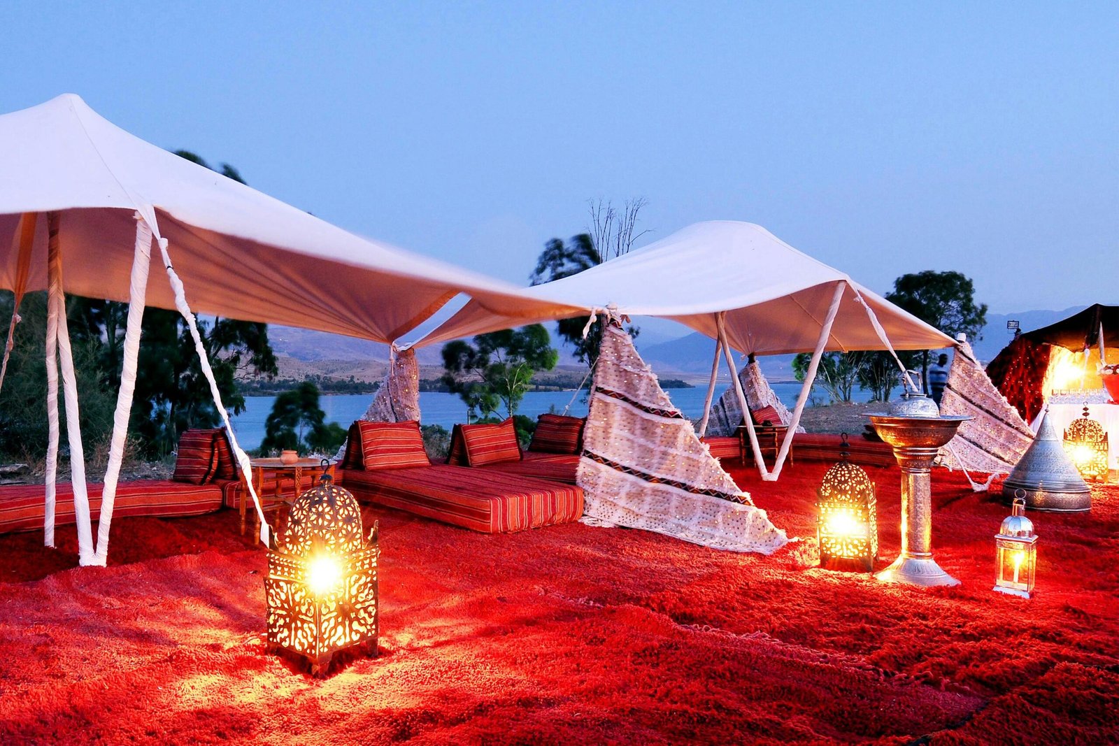 Traditional Moroccan tent setup with lanterns by the lakeside at twilight in Ouarzazate.